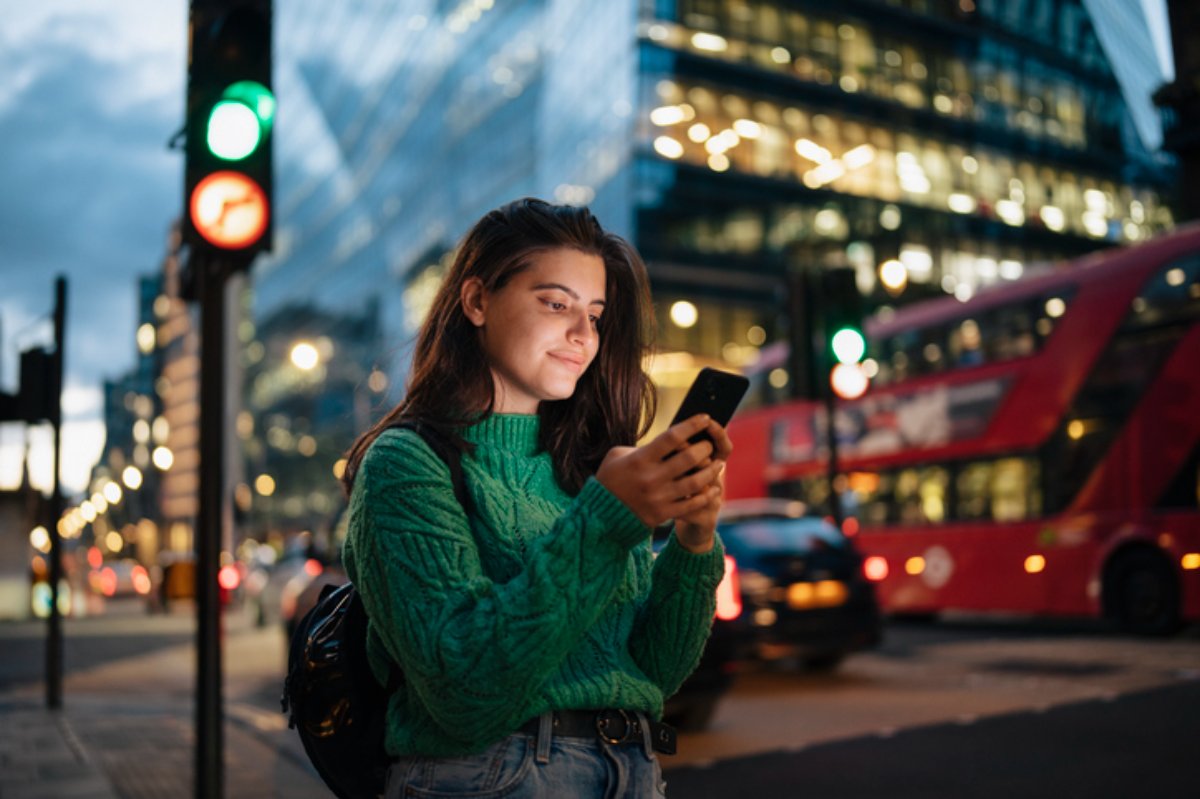 A woman checking her phone on a London street at dusk
