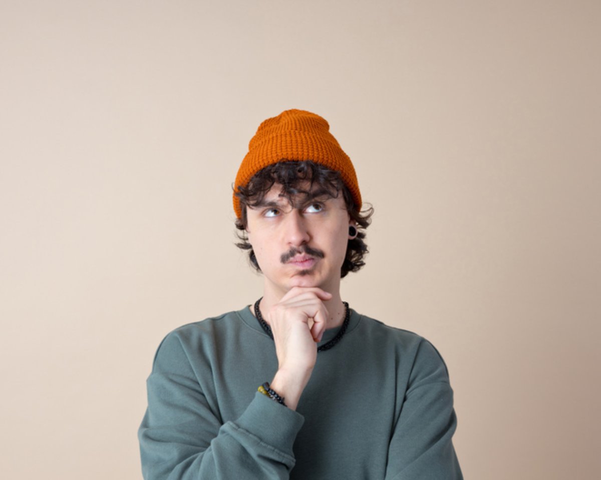 A man in a beanie looking upward, thinking