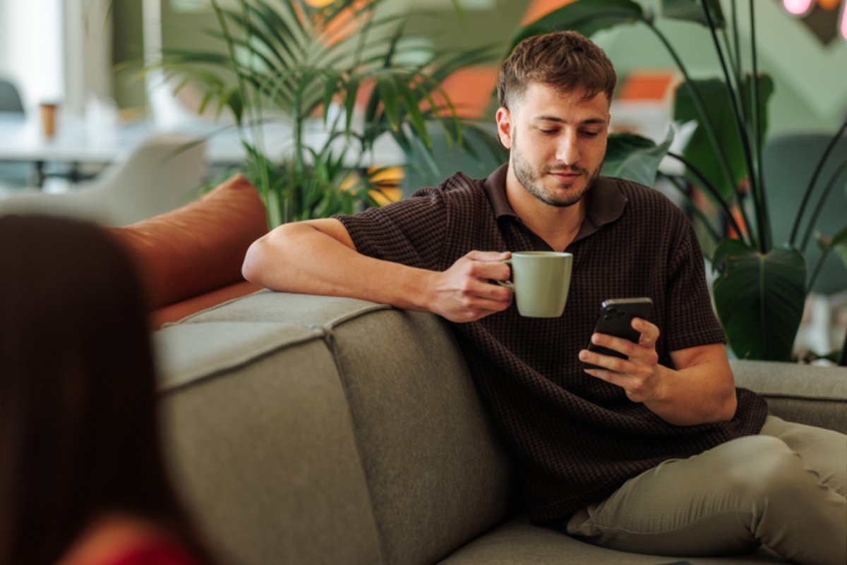 A man on a sofa with a coffee, checking his phone