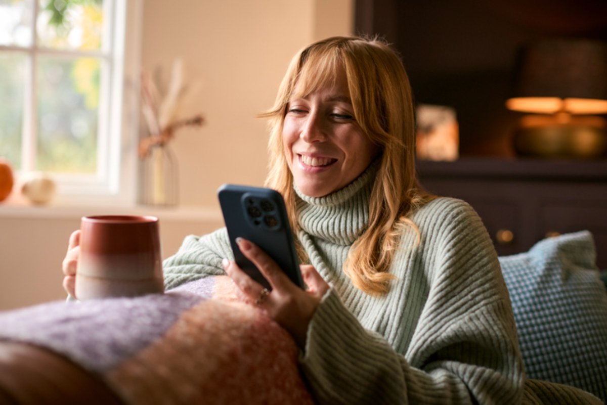 A woman on a sofa with a mug, reading something on her phone
