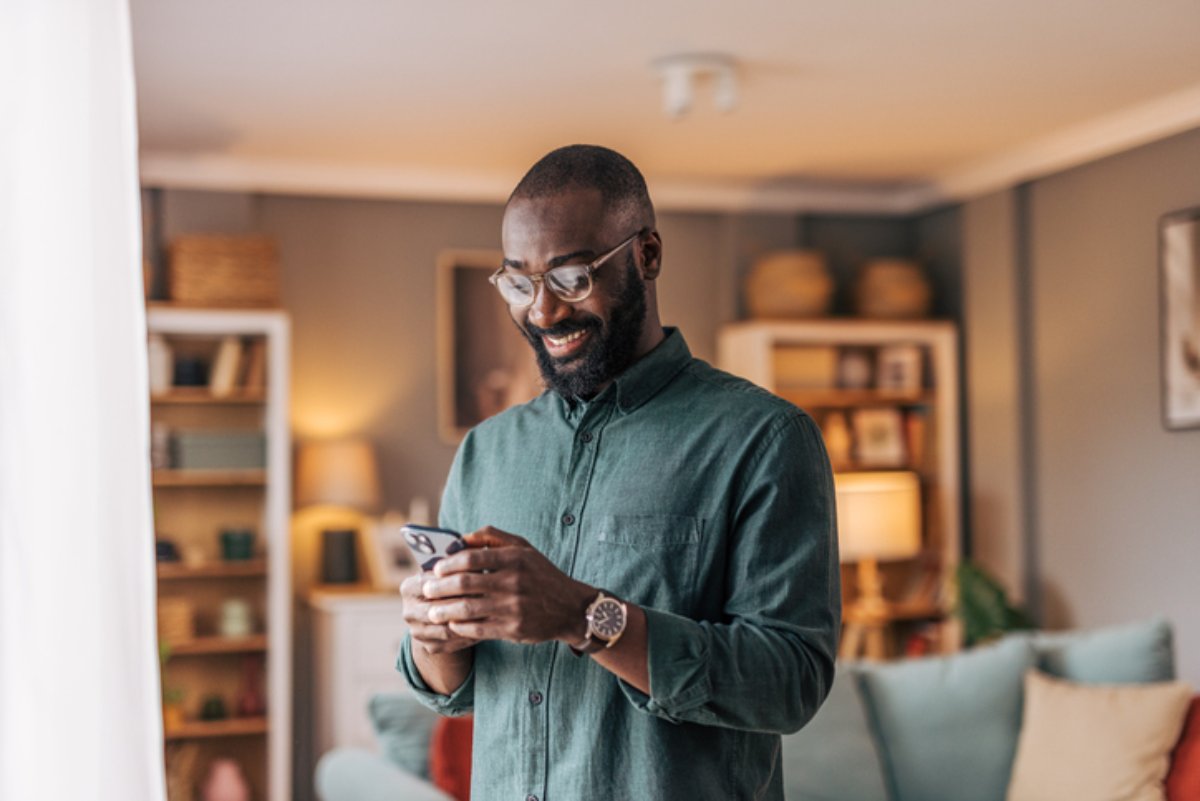 A man standing in his living room, smiling at his phone