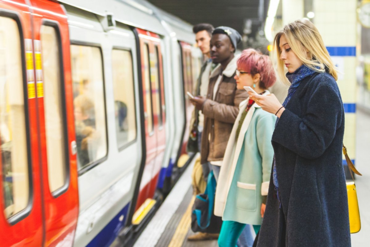 Commuters on a London Underground platform, checking their phones